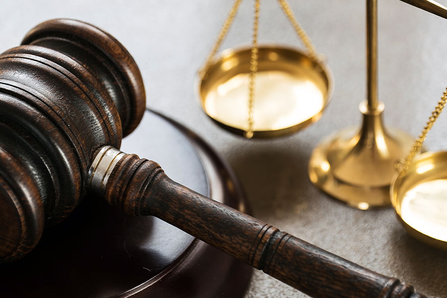 Close-up of a wooden gavel on a sound block with brass scales of justice in the background.