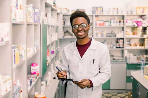 Smiling African American man pharmacist Writing On Clipboard While standing in interior of pharmacy