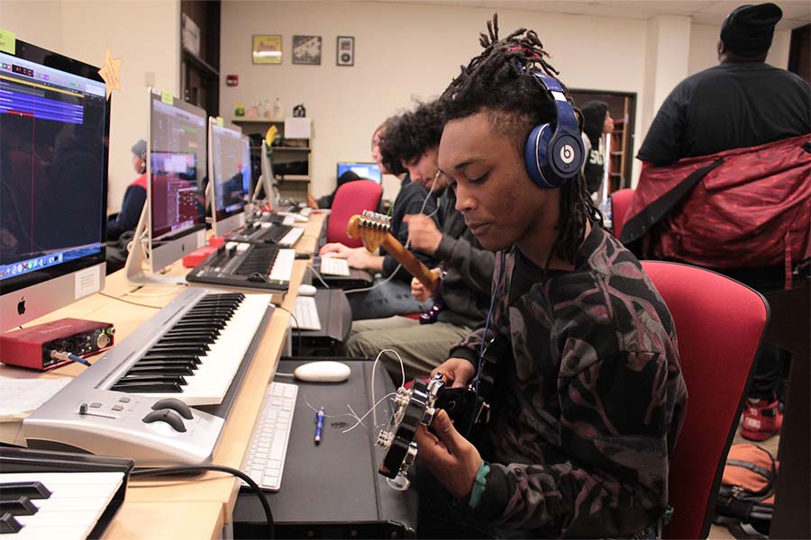 Students with guitars sit at keyboard and computer screen