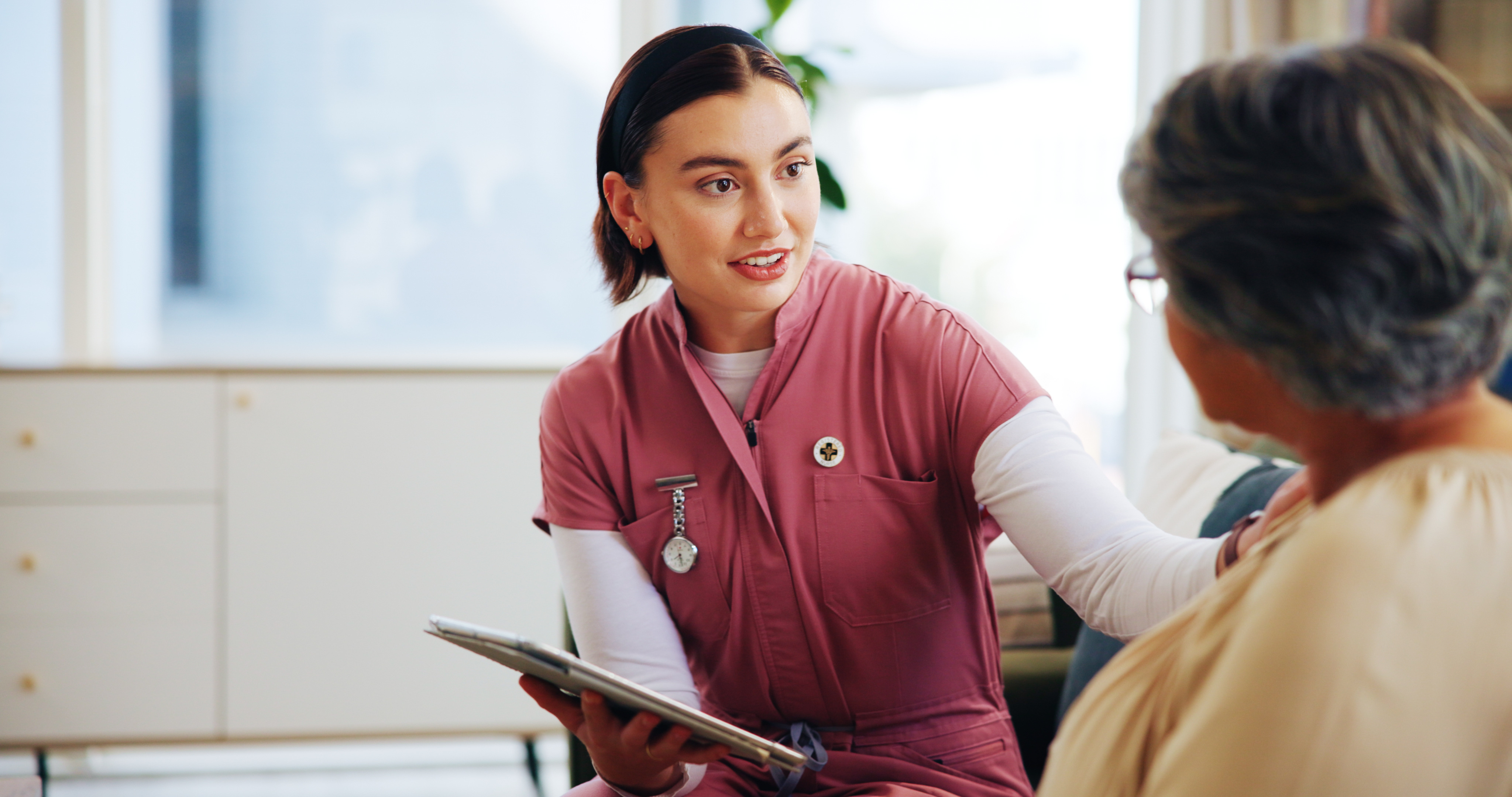 female patient care tech sitting and talking to a patient with a clipboard