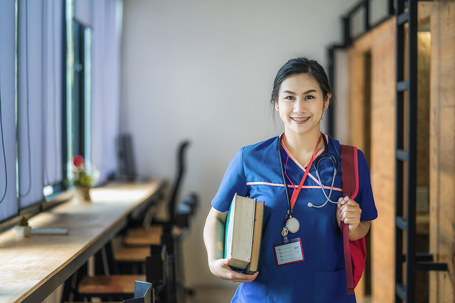 female nursing student in blue scrubs holding files and smiling