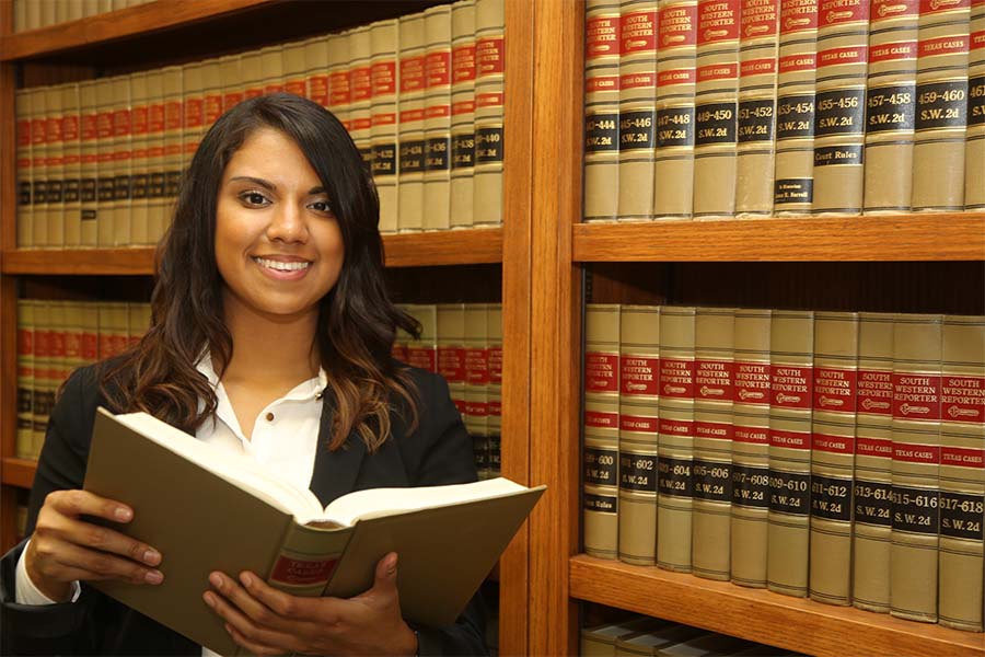 Person stands in front of shelves filled with legal books, holding an open book.